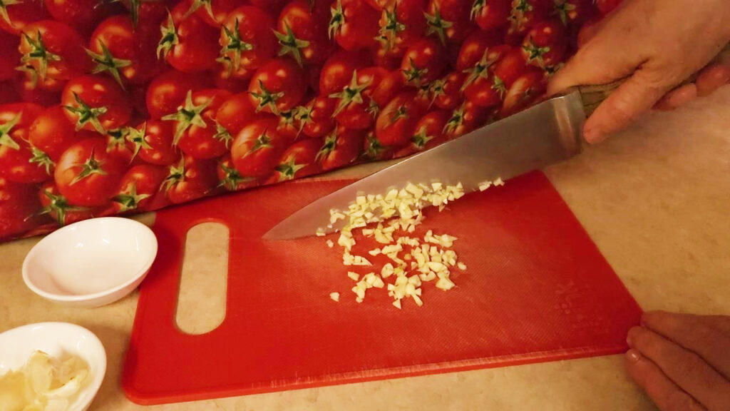 this image shows garlic being chopped on a red cutting board